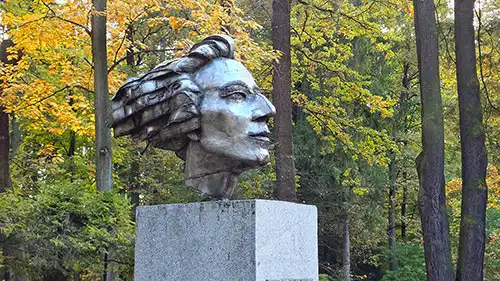 Nowoczesny pomnik Fryderyka Chopina na kamiennym postumencie, otoczony jesiennym parkiem krajobrazowym w Antoninie.