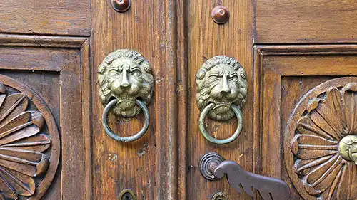 Drewniane drzwi wejściowe Pałacu Myśliwskiego Radziwiłłów z dwiema zabytkowymi kołatkami w kształcie lwich głów.