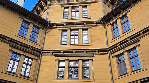 Zbliżenie na drewnianą fasadę Pałacu w Antoninie z perspektywy z dołu, ukazujące szczegółową strukturę i rzędy okien.