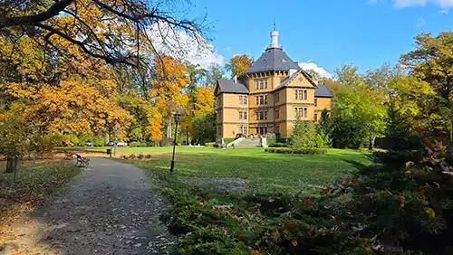 Pałac Myśliwski Radziwiłłów Antonin widziany znad ścieżki w jesiennym parku, z dużym trawnikiem przed budynkiem.