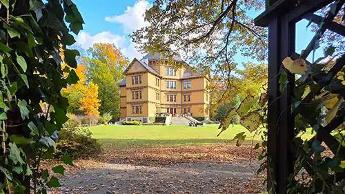Pałac Radziwiłłów w Antoninie widziany przez drewnianą ramę, jesienne liście na pierwszym planie, rozległy park z trawnikiem.