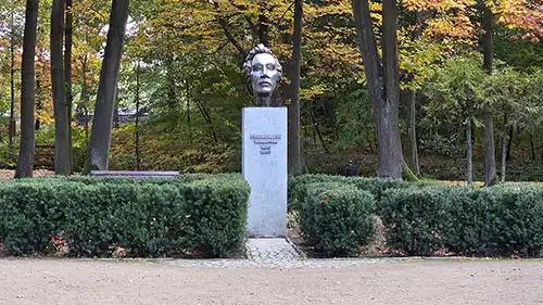 Pomnik Fryderyka Chopina na wysokim, jasnym postumencie, otoczony geometrycznym żywopłotem w parku Antonin.