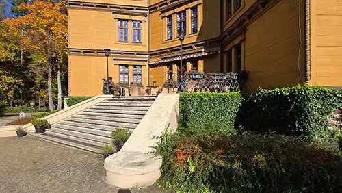 Kamienne schody prowadzące do wejścia Pałacu Radziwiłłów w Antoninie, otoczone zielonym żywopłotem i jesienną roślinnością.