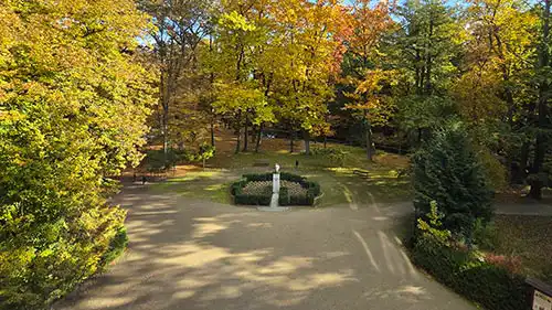 Widok z okna Pałacu Radziwiłłów w Antoninie na park, centralny klomb z rzeźbą na tle jesiennych drzew o ciepłych kolorach.