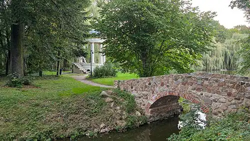 Kamienny mostek nad kanałem w parku pałacowym w Dobrzycy. W tle widoczny Monopter.