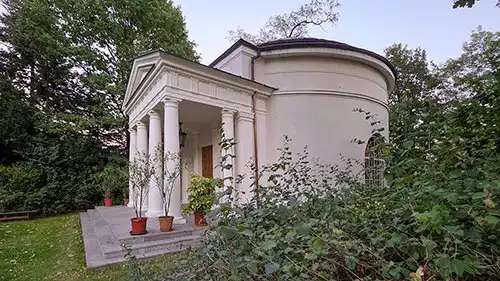 Panteon w Dobrzycy. Klasycystyczna budowla z portykiem kolumnowym ujęta z boku, otoczona roślinnością.