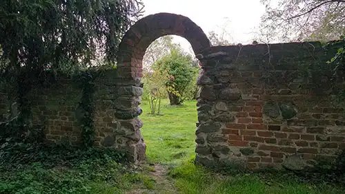 Fragment romantycznego muru z cegły i kamienia z łukową bramą w parku pałacowym w Dobrzycy.