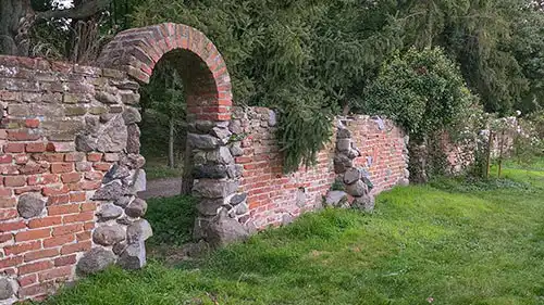 Brama w postaci łuku w stylizowanym na ruinę murze z kamienia i czerwonej cegły, w parku w Dobrzycy.