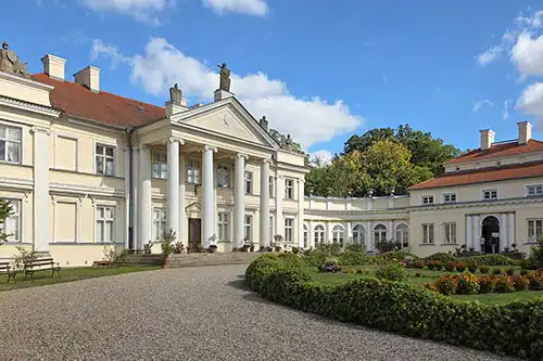 Klasycystyczna fasada Pałacu w Śmiełowie z kolumnowym portykiem i klombem z kwiatami, widok główny.