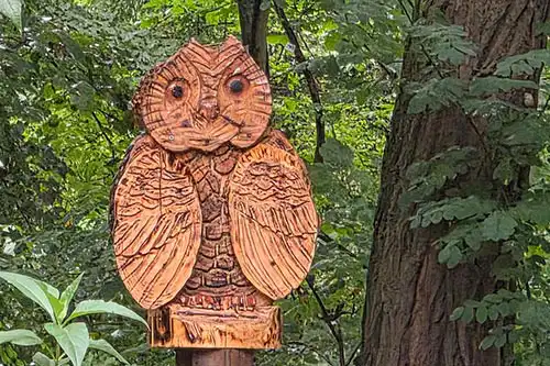 Drewniana rzeźba sowy w zabytkowym parku Pałacu Śmiełów, ukryta wśród drzew i zieleni parkowej.